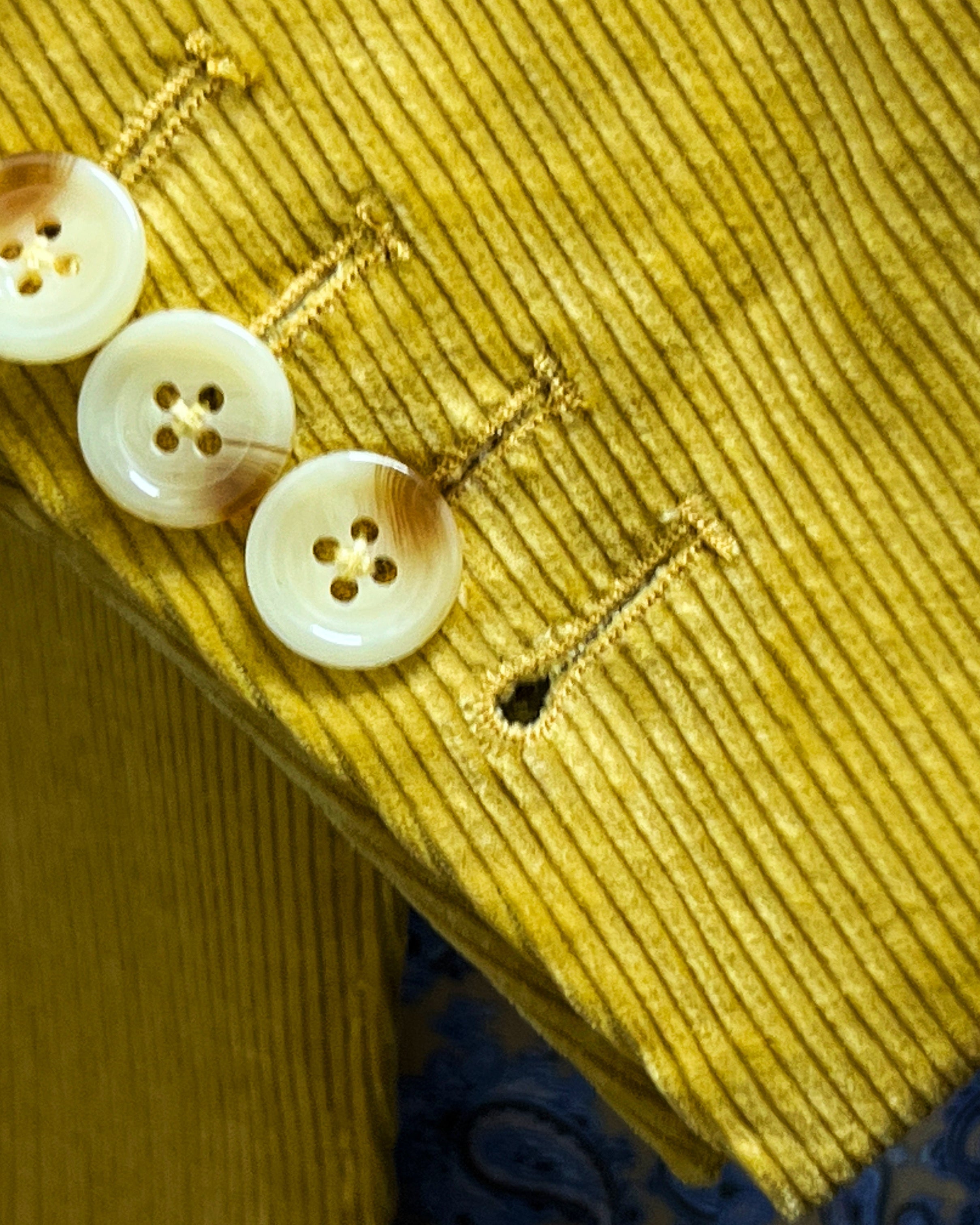 Sport coat sleeve cuff showing functional buttonholes with hand-finished stitching on warm mustard yellow corduroy fabric