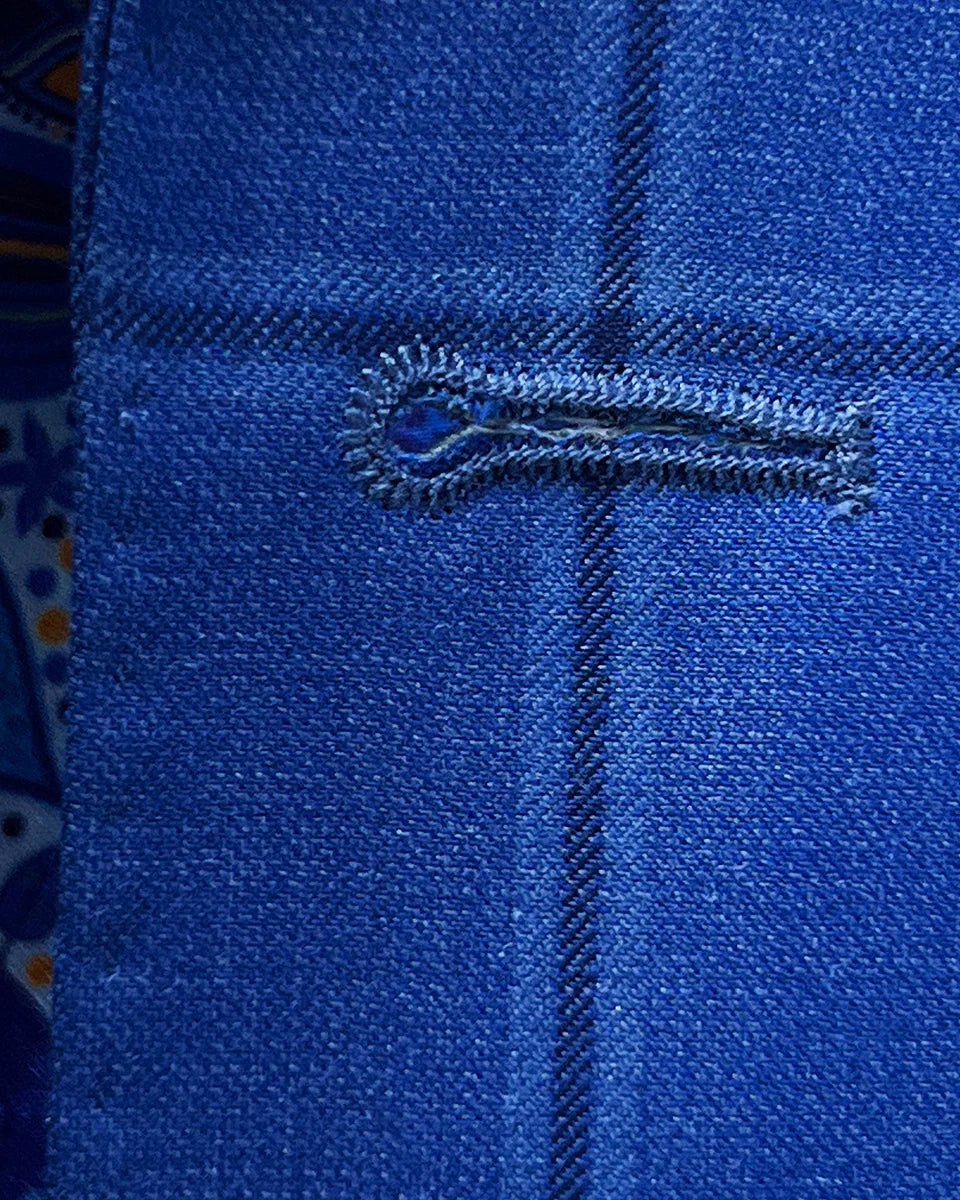Detailed macro shot of hand-finished buttonhole stitching on royal blue windowpane suit with dark blue contrast thread