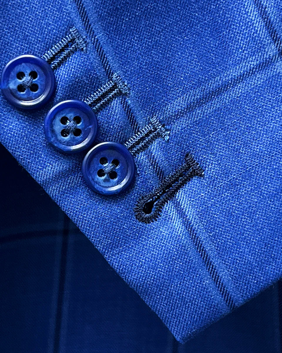 Suit jacket sleeve cuff showing functional buttonholes with contrast dark blue accent stitching on royal blue windowpane fabric
