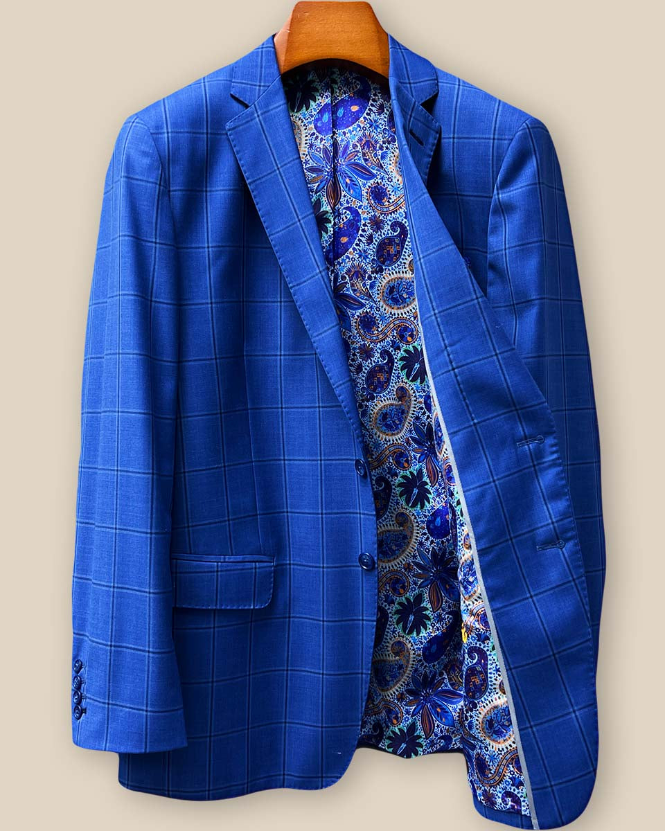 Interior left side of royal blue windowpane suit jacket displaying light blue, navy and gold paisley lining with inner pocket