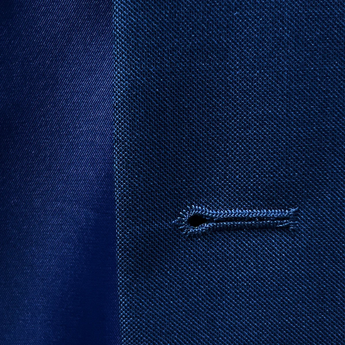 Close-up view of the meticulous buttonhole stitching on the cobalt blue sharkskin suit.