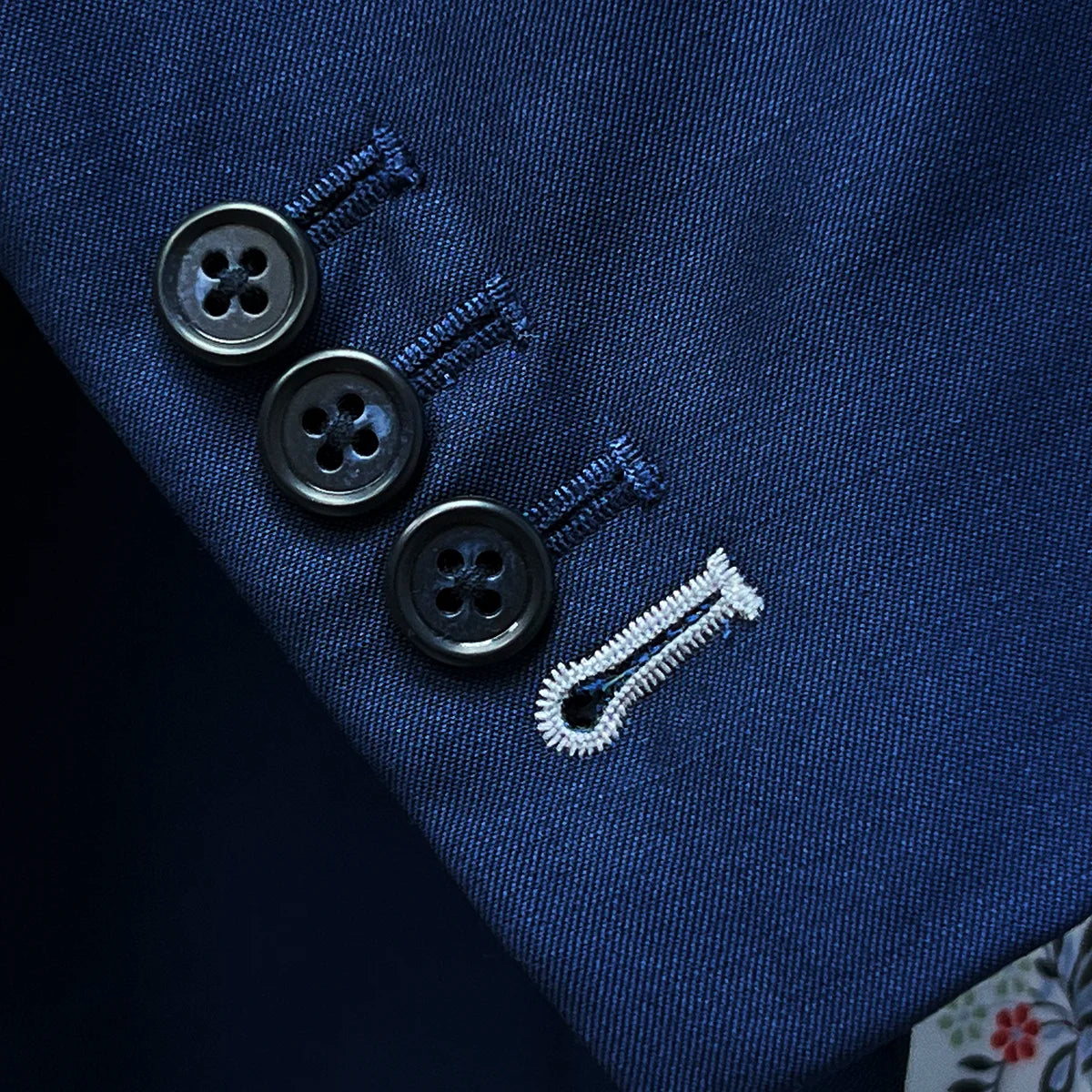 Detailed view of suit jacket sleeve, showing functional buttonholes with white contrast stitching