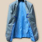 Full inside view of the light grey suit jacket highlighting the sky blue bemberg silk lining with royal blue contrast piping.