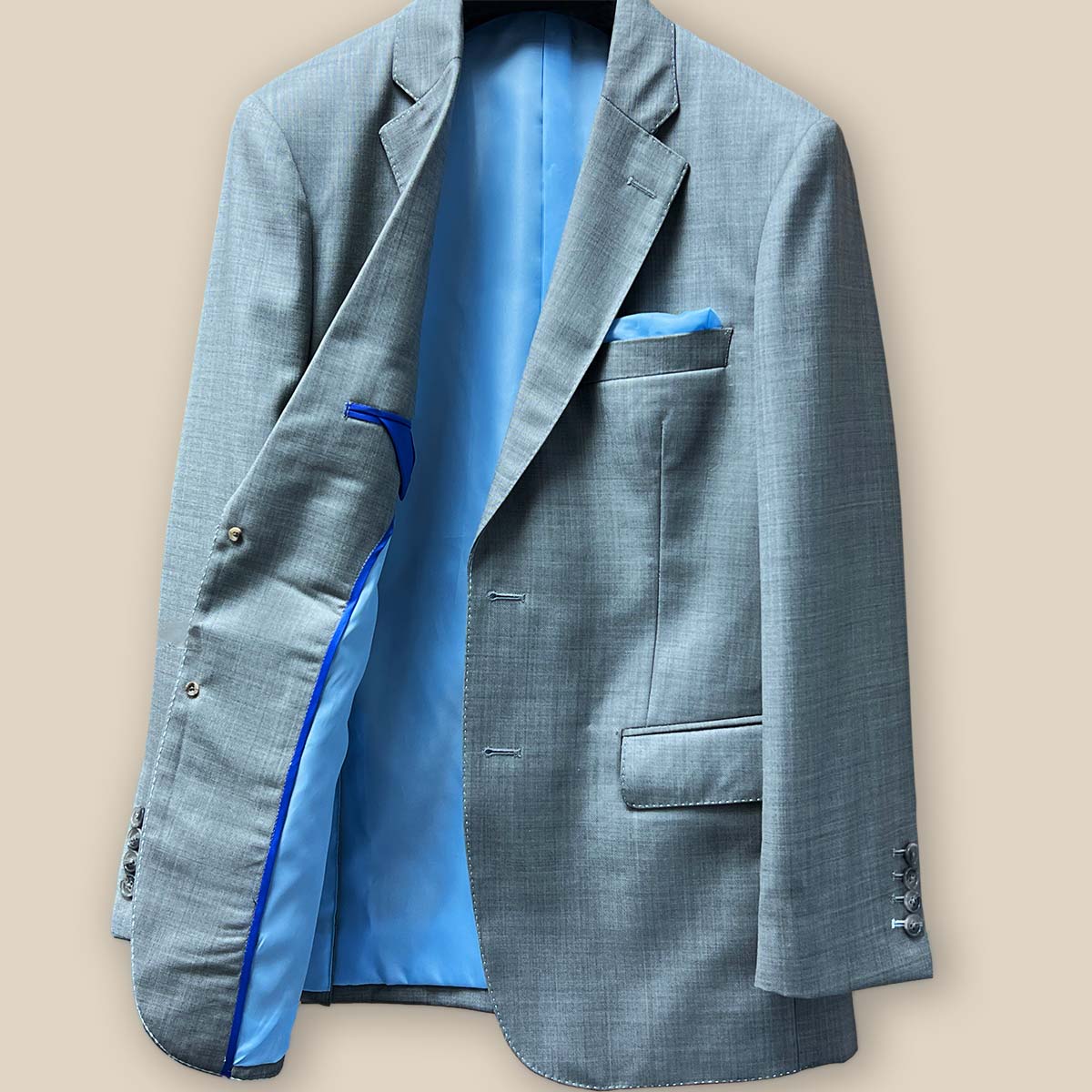 Inside right view of the light grey suit jacket featuring the sky blue bemberg silk lining and royal blue contrast piping.