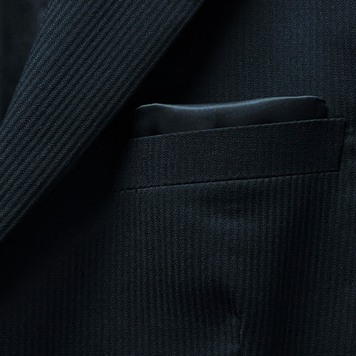 View of the built-in pocket square in the jacket's pocket, complementing the black herringbone fabric.