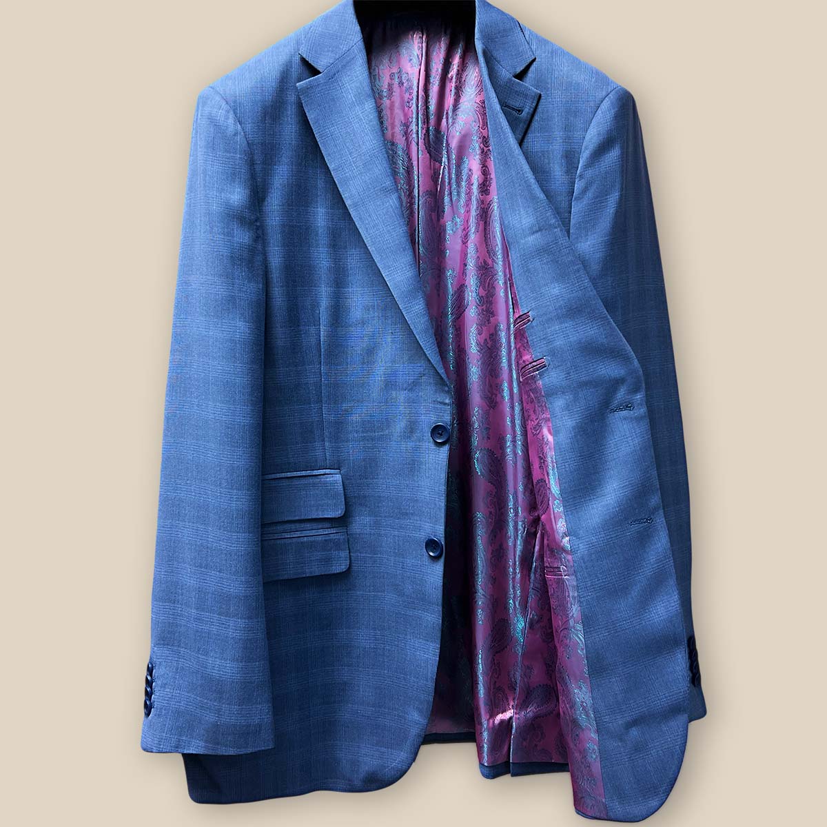 The inside left view of a medium blue Prince of Wales glen plaid suit jacket, showcasing the pink and purple iridescent paisley lining.