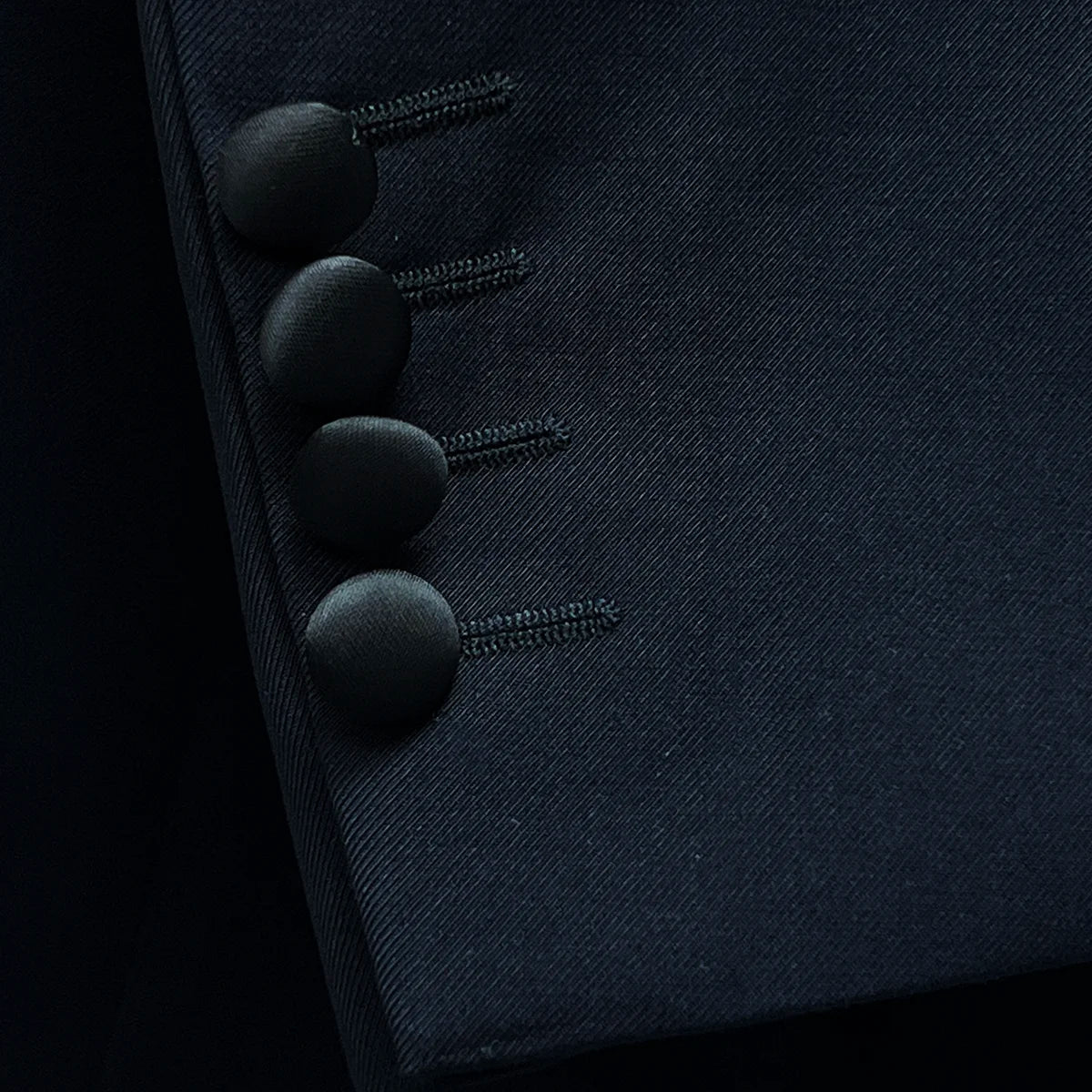 Detail of the functional sleeve buttonholes, showcasing the black satin-covered buttons and precise stitching.