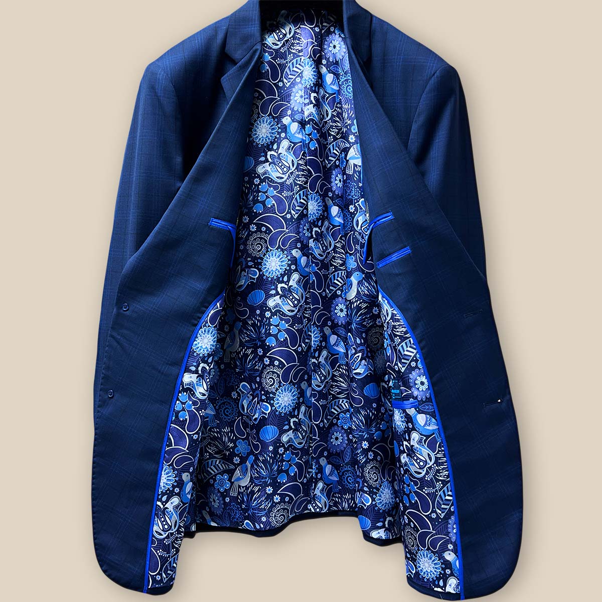 Full view of the interior lining of the dark blue windowpane men's sport coat with blue and white aviary motif flash lining and royal blue piping.