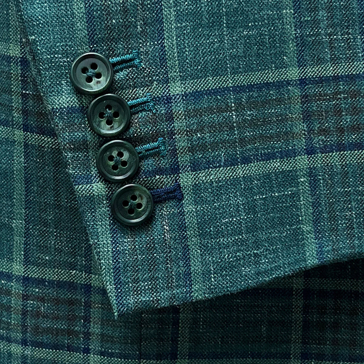 Functional sleeve buttonholes on the Westwood Hart hunter green with navy and chocolate brown plaid mens sport coat, with navy blue contrast accents on the last buttonhole.