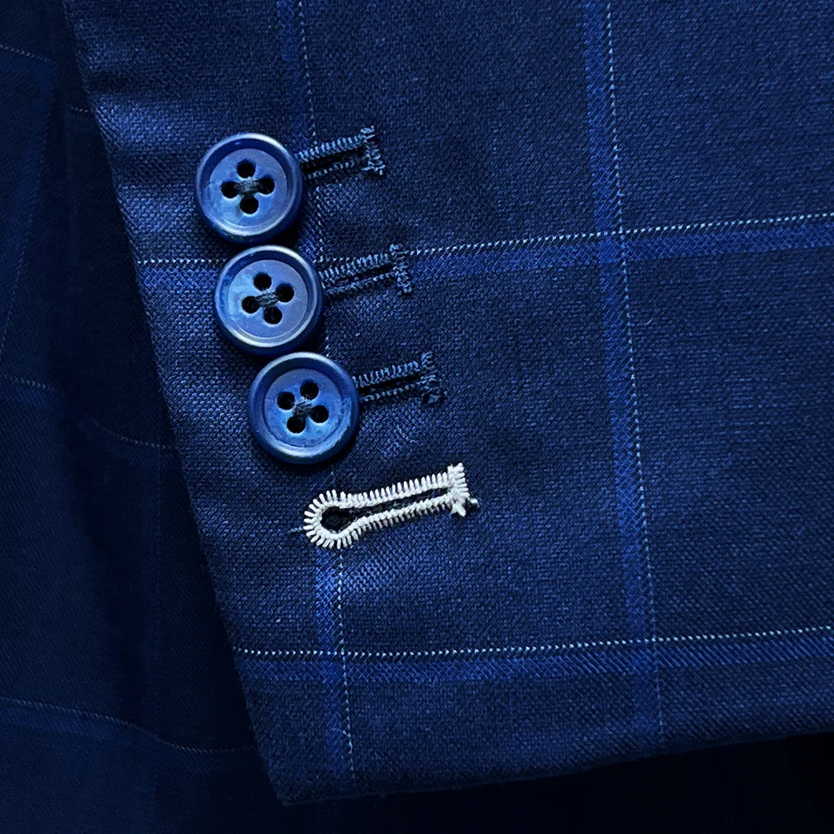 Close-up of the functional sleeve buttonholes with white contrast stitching on the royal blue suit fabric.
