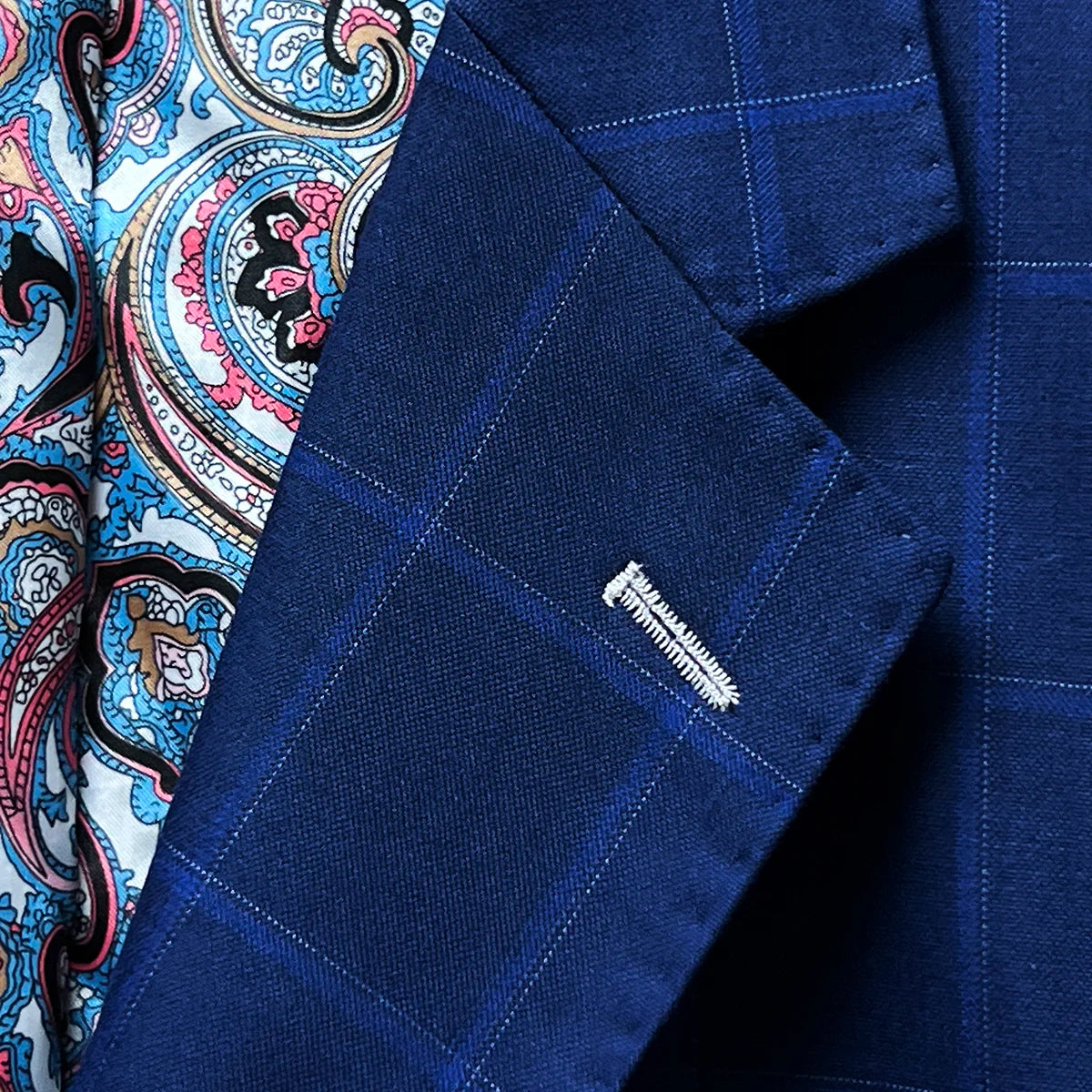 Close-up of the notch lapel with hand pick stitching on the royal blue fabric featuring a navy and white windowpane pattern.