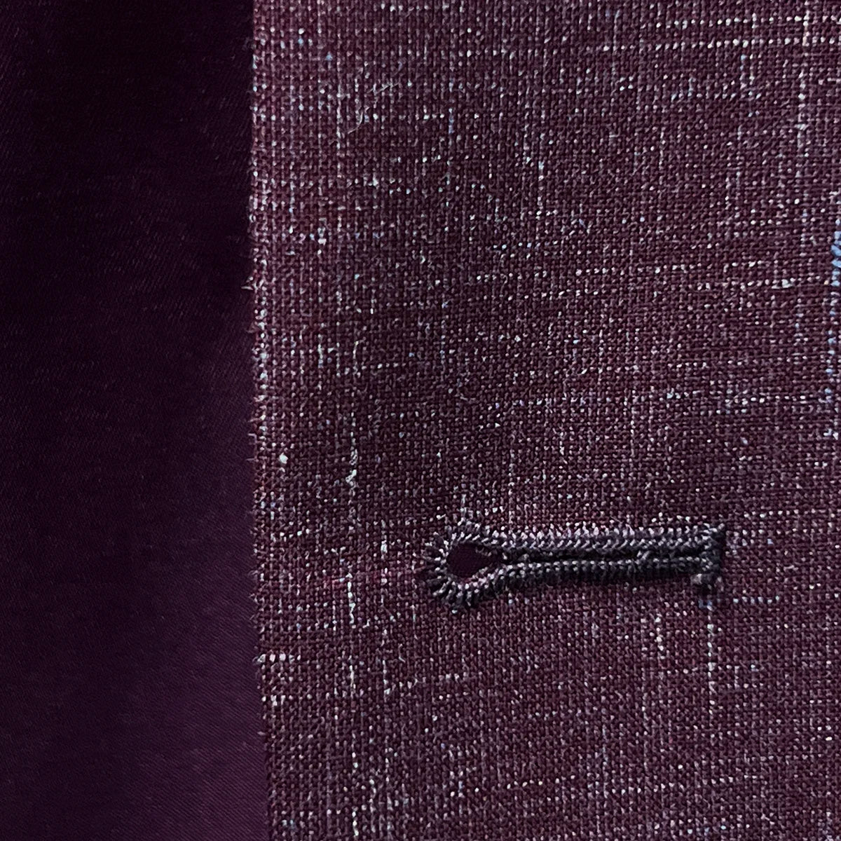 Close-up of the buttonhole stitching on a cranberry men's suit by Westwood Hart, showcasing precise tailoring.