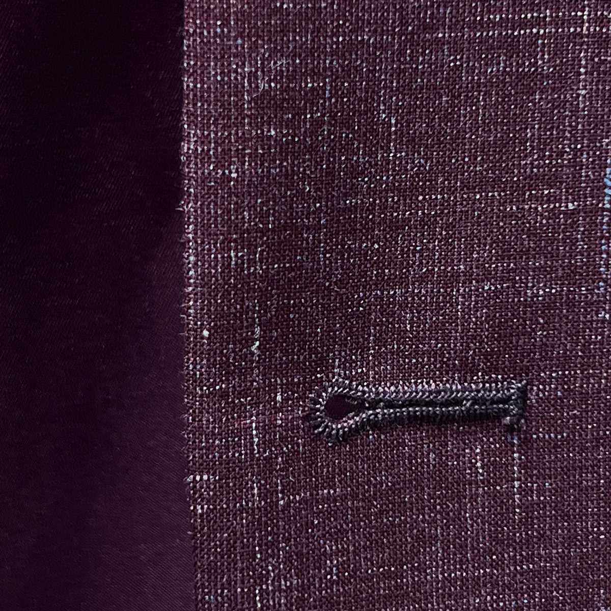 Close-up of the buttonhole stitching on a cranberry men's suit by Westwood Hart, showcasing precise tailoring.