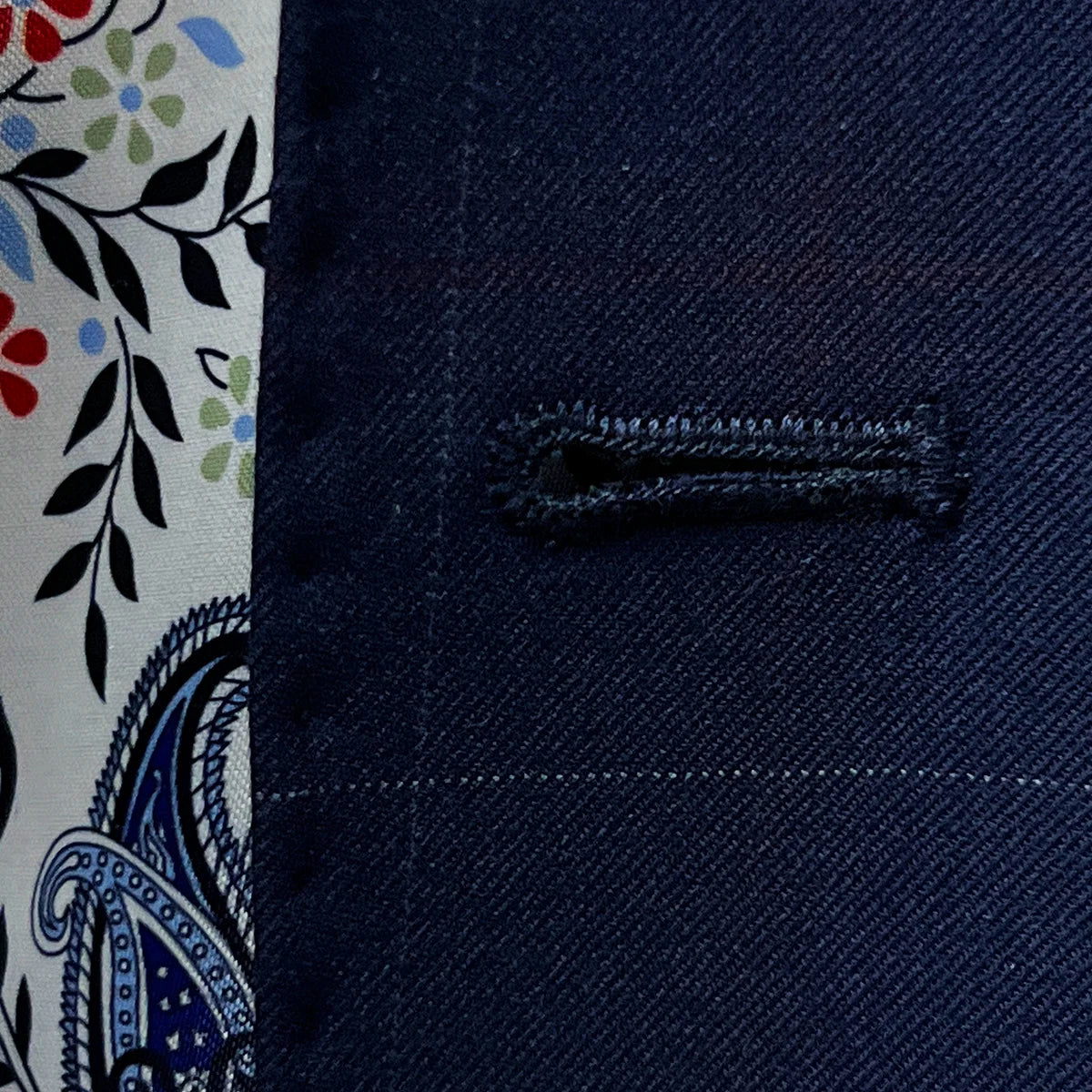 Macro view of the precise white contrast buttonhole stitching showing the quality handwork on the navy wool fabric