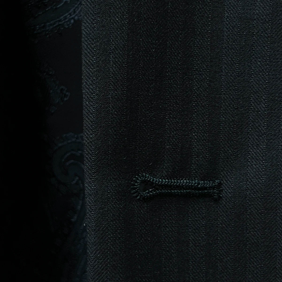Close-up of a buttonhole on the black herringbone suit.