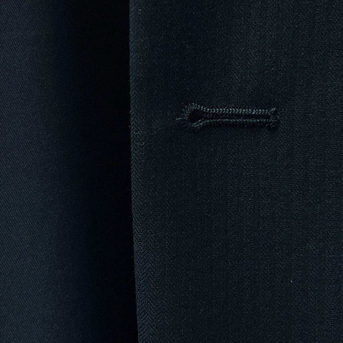 Close-up of the intricate buttonhole detail on black herringbone fabric.
