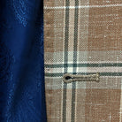 Close up view of buttonhole craftsmanship on a brown beige men's sport coat with blanched almond and midnight blue windowpane pattern.