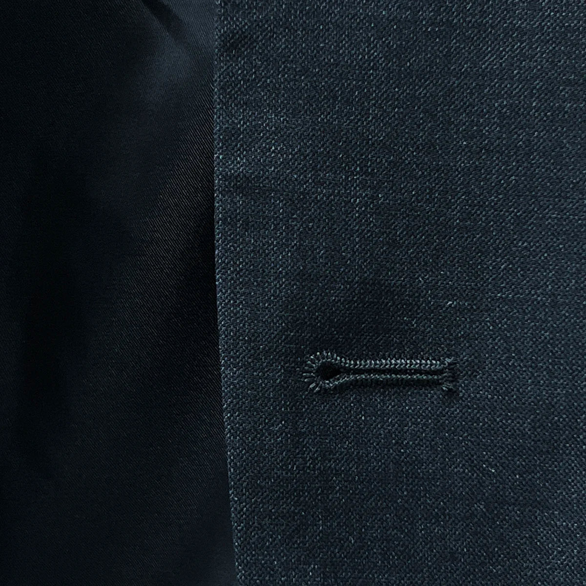 Close-up view of buttonhole detailing on a dark gray sharkskin suit.