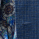 Close up view of the meticulously crafted buttonhole on a gray blue mini grid checks sport coat made of flannel wool.