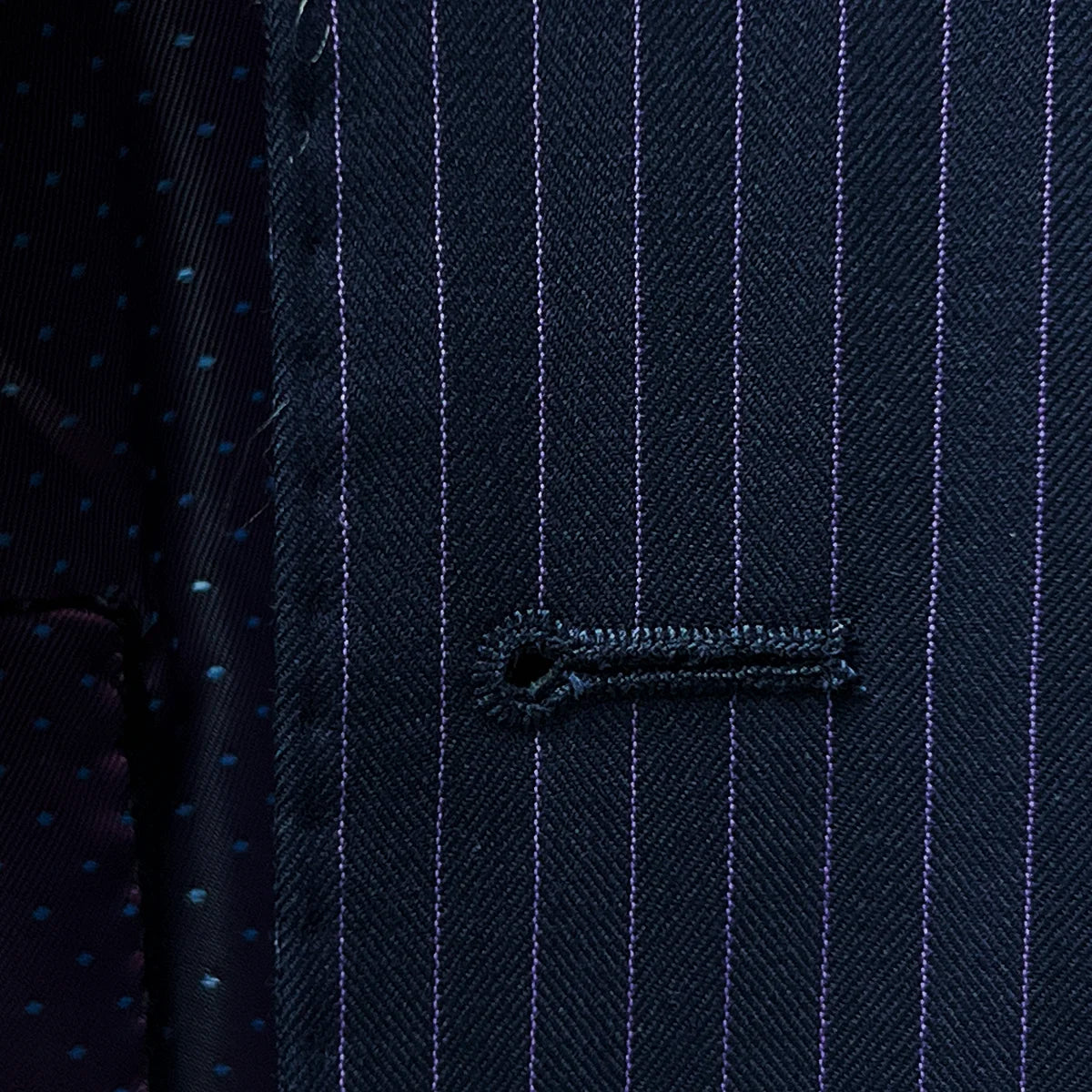 Close-up view of a buttonhole, a fine detail on a navy suit with purple pinstripes.