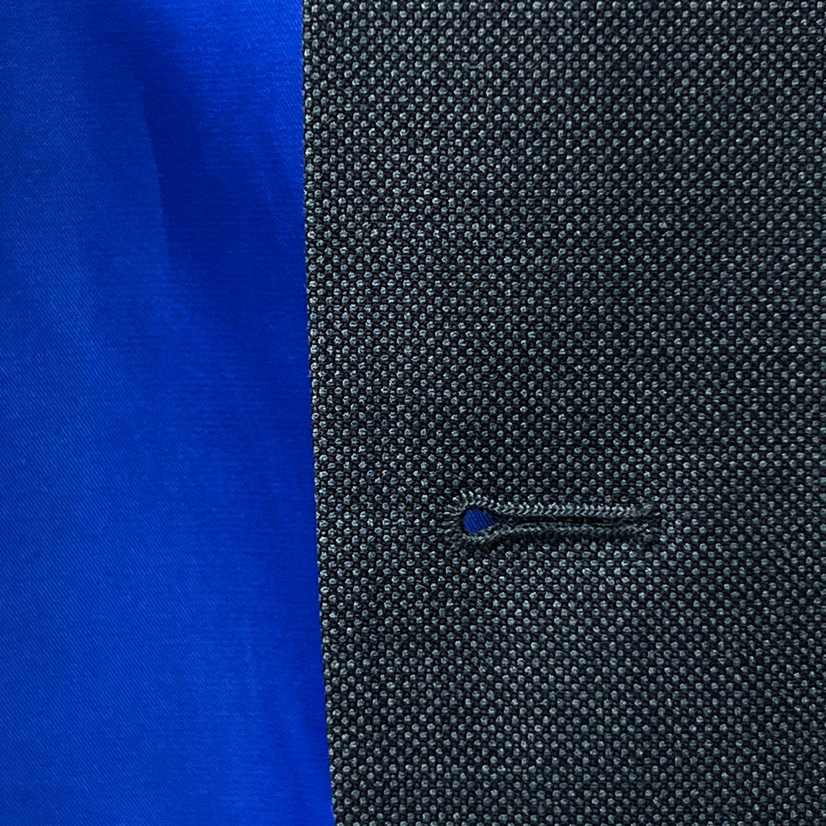 Close-up of the jacket buttonhole panel illustrating the finesse in tailoring of a dark grey birdseye suit.