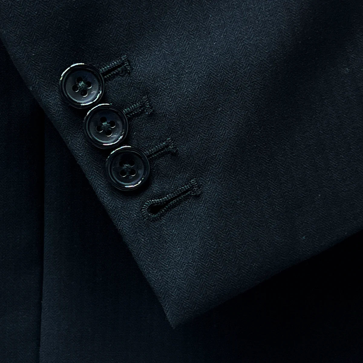 Functional sleeve buttonholes on a tailored black herringbone suit.