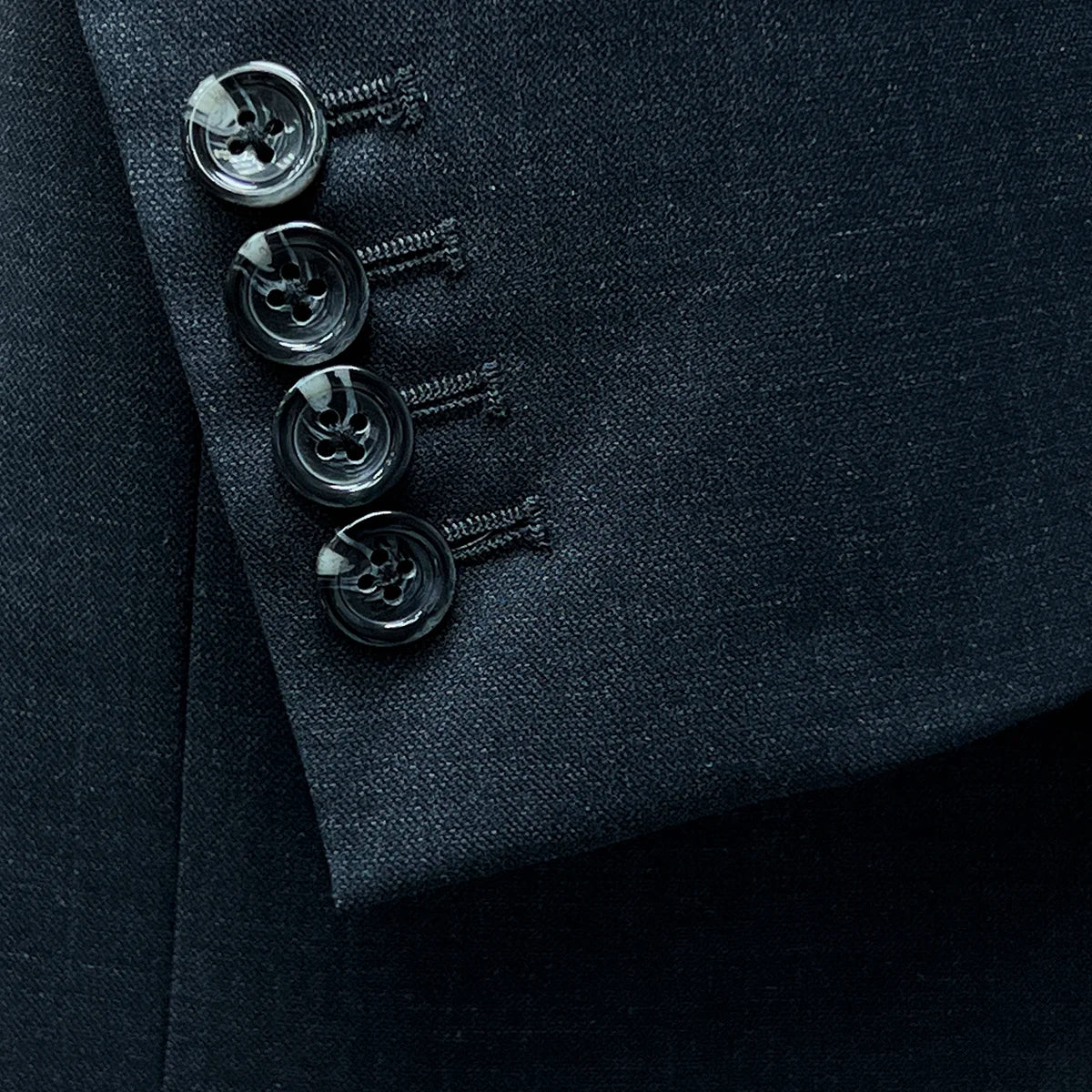 Functional sleeve buttonholes demonstrating practical design on a dark gray sharkskin suit.