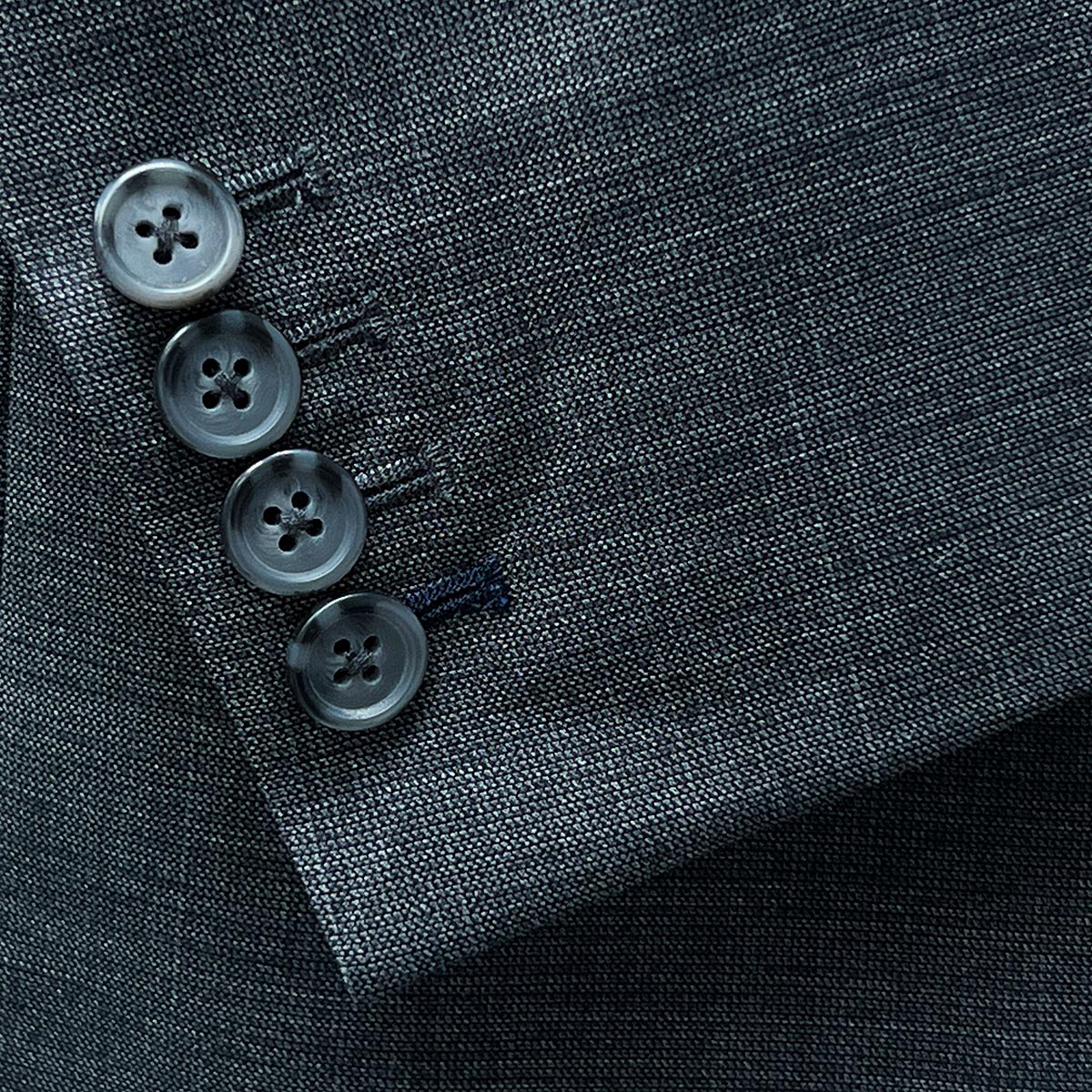 Functional sleeve buttonholes allowing for easy adjustment on a dark grey nailhead suit.