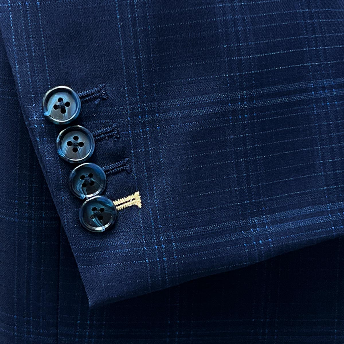 Functional sleeve buttonholes allowing for precise sleeve length adjustment on a midnight blue windowpane suit.
