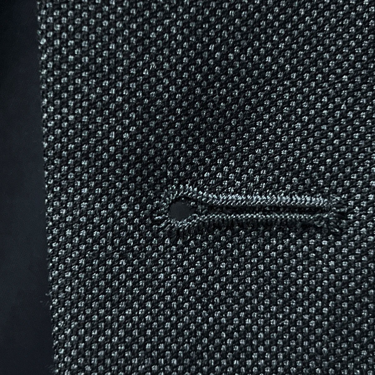 Macro detail of buttonhole stitching showing precise tailoring on dark grey birdseye fabric