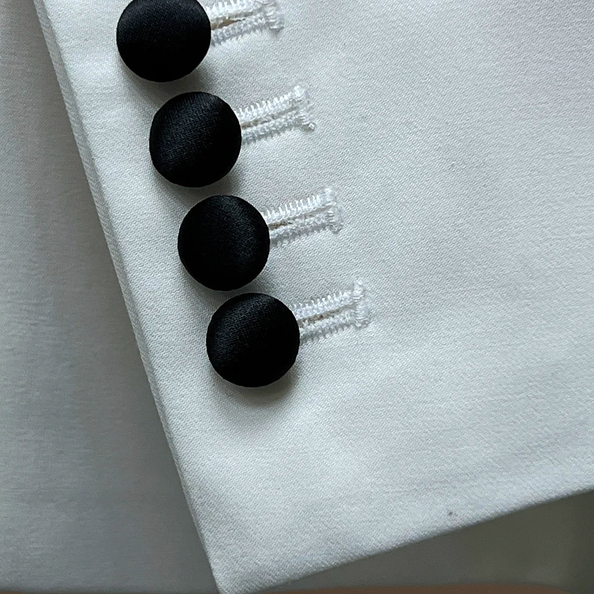Close-up of the functional sleeve buttonholes on the ivory tuxedo jacket, featuring black satin covered buttons.