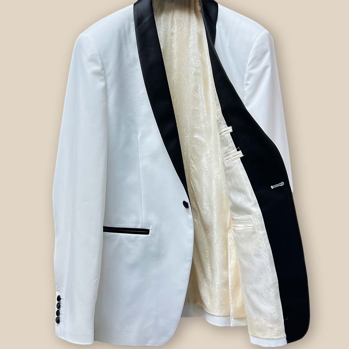 Inside view of the left side of the ivory tuxedo jacket showcasing the off white paisley lining and inner pocket.