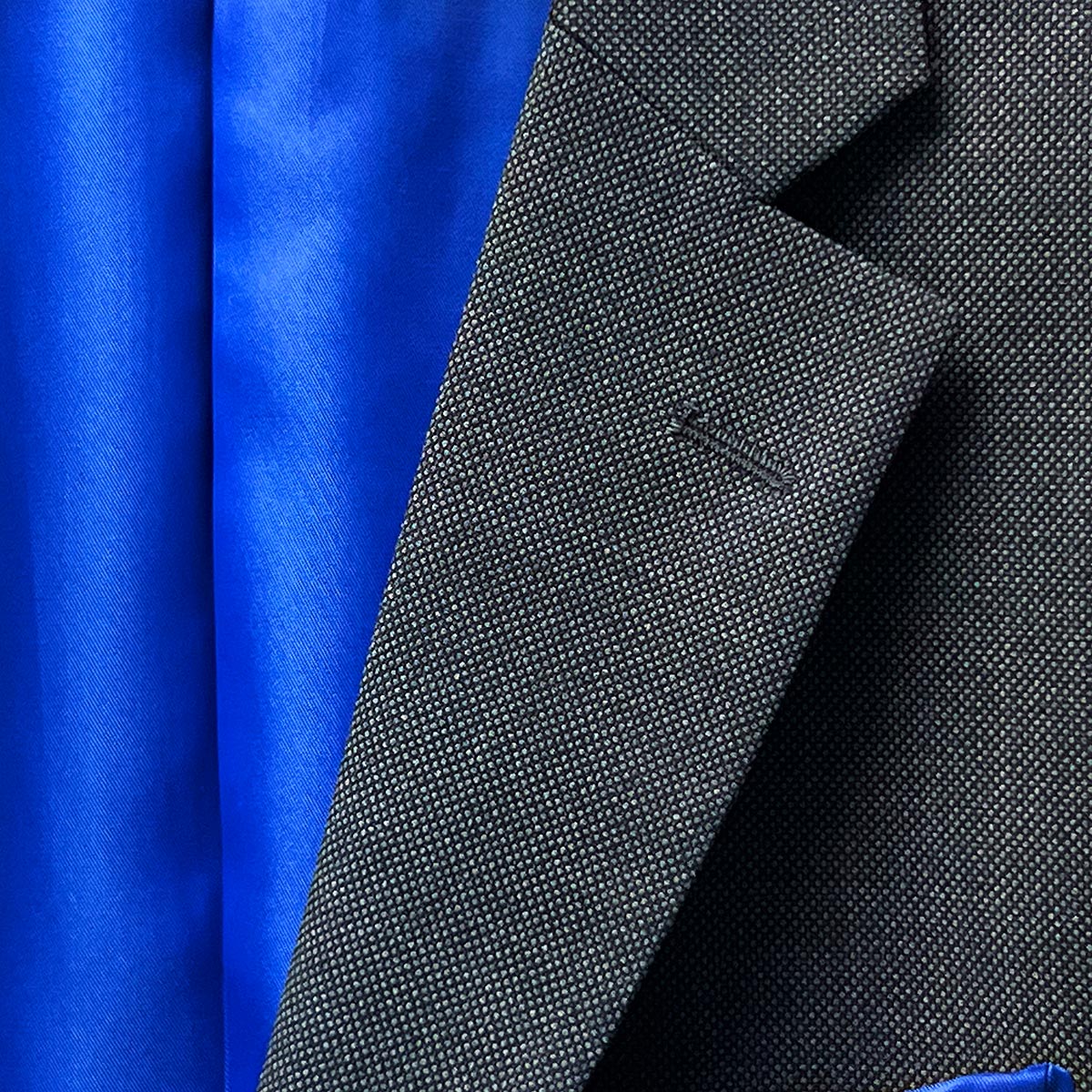 A well-designed lapel buttonhole signifying attention to detail on a dark grey birdseye suit.