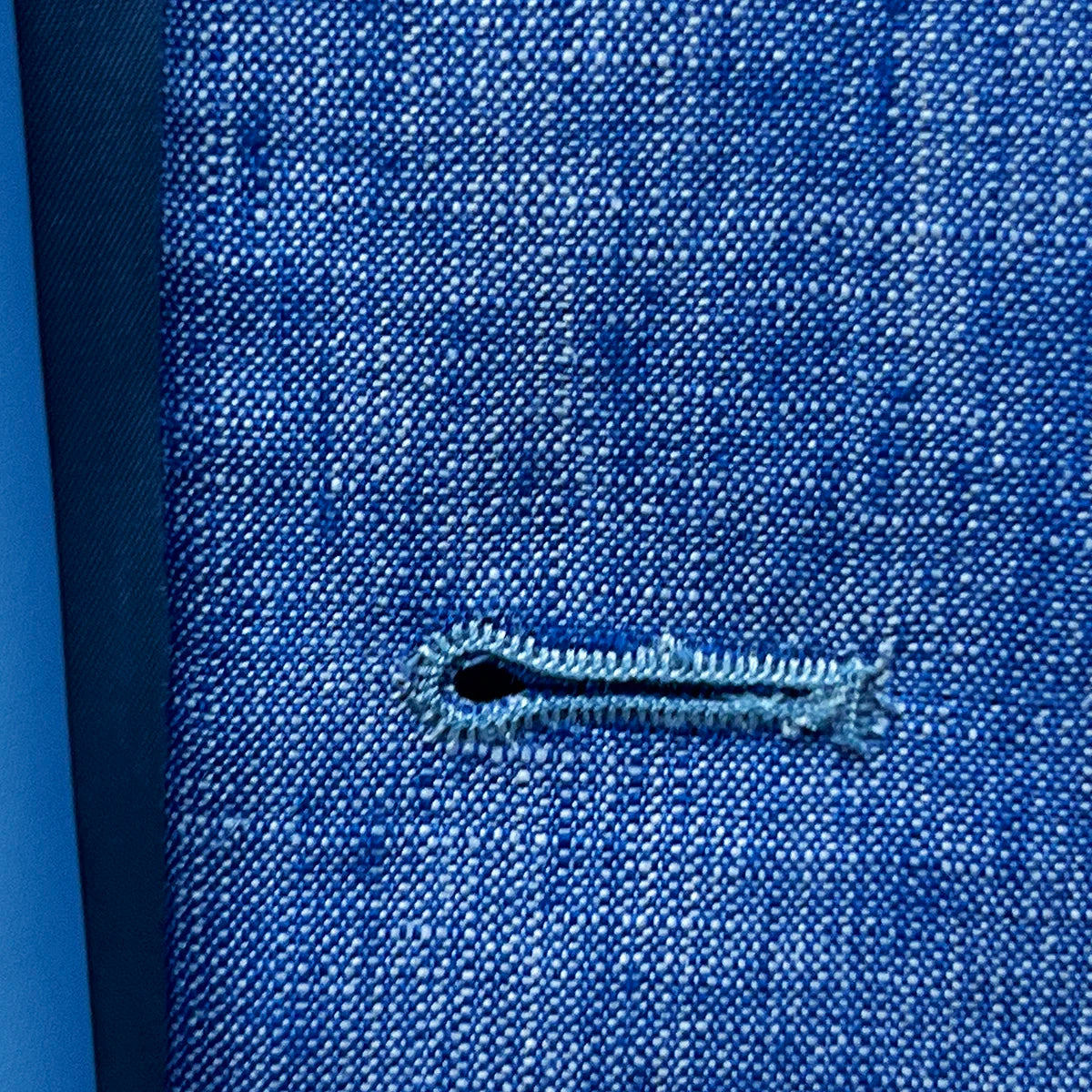 Macro shot of buttonhole stitching on light blue solid Irish linen men's suit, highlighting quality craftsmanship
