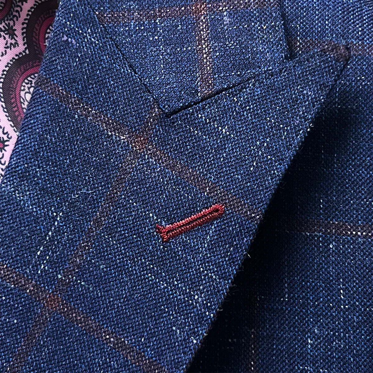 Detailed view of peak lapel construction on navy windowpane sport coat featuring ruby red contrast buttonhole and hand-picked edges