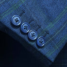 Suit jacket sleeve cuff showing functional buttonholes with contrast navy accent stitching on deep blue overcheck fabric