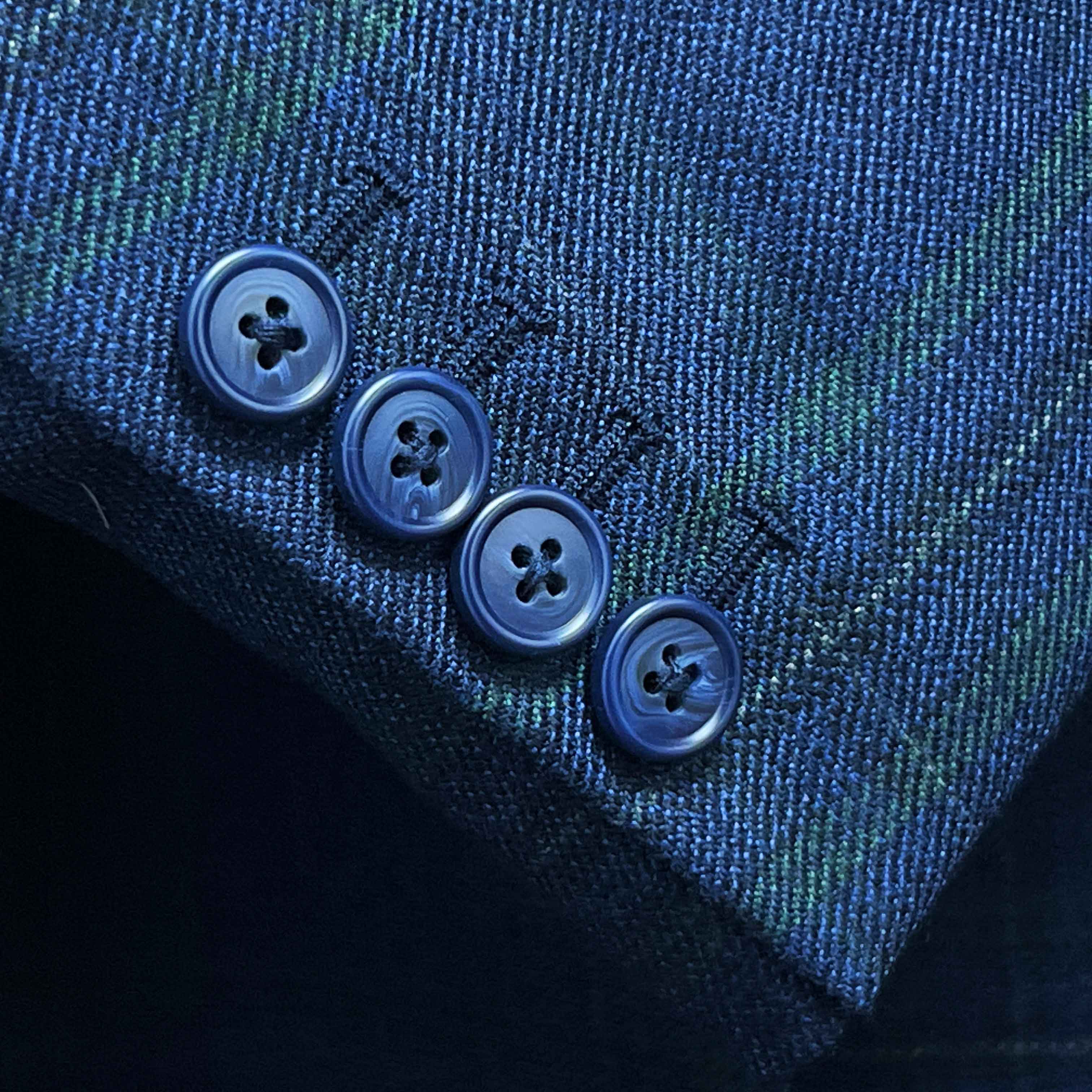 Suit jacket sleeve cuff showing functional buttonholes with contrast navy accent stitching on deep blue overcheck fabric