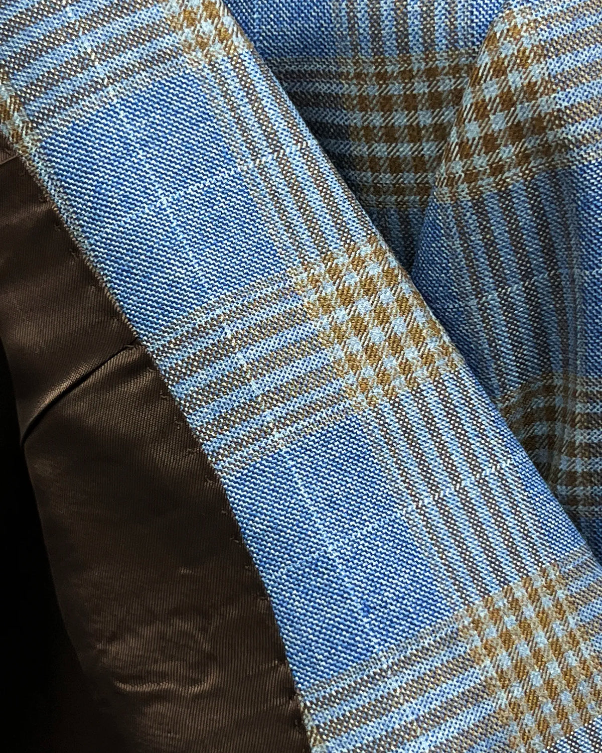 Fabric texture detail of light blue with tobacco brown glen check men's sport coat showing the cloth surface