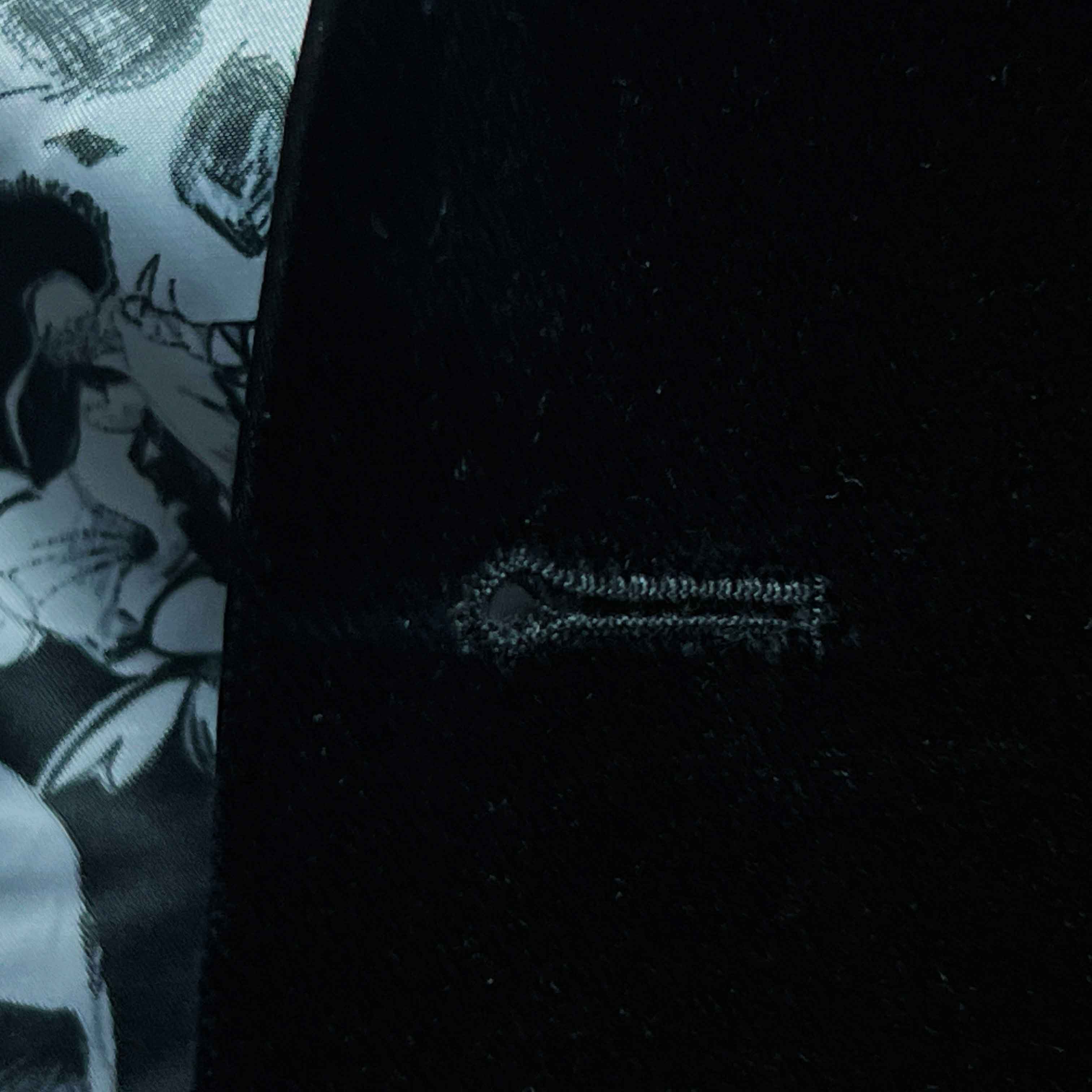 Detailed macro shot of hand-finished buttonhole stitching on black silk velvet formalwear tuxedo with contrast thread