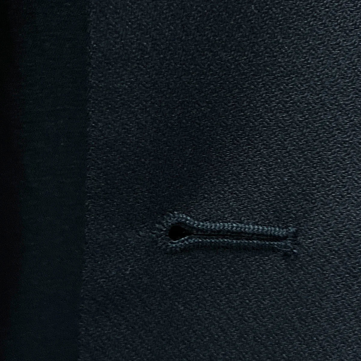 Macro view of precise buttonhole stitching on a black self-textured jacquard suit