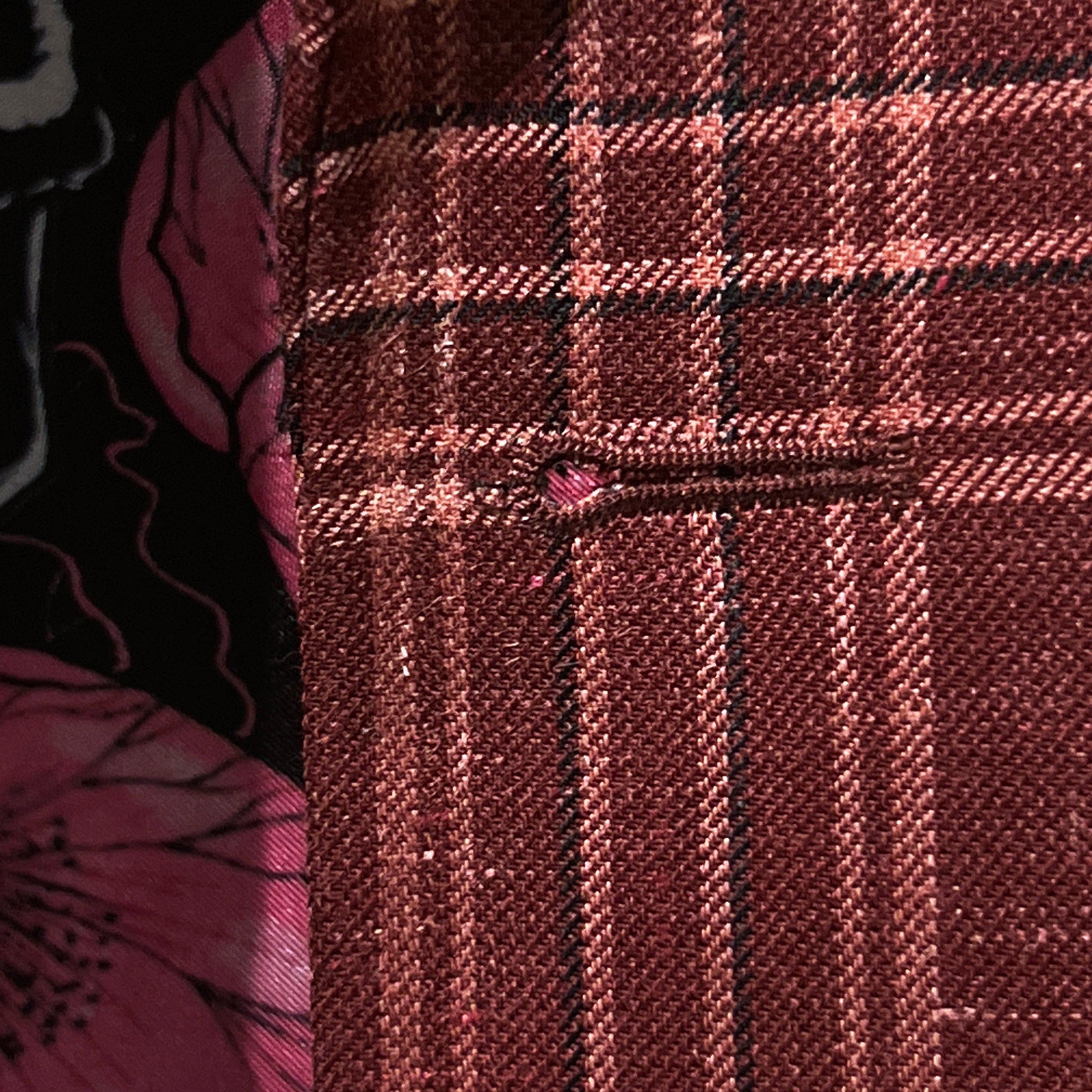 Detailed macro shot of hand-finished buttonhole stitching on burgundy plaid sport coat with white contrast thread