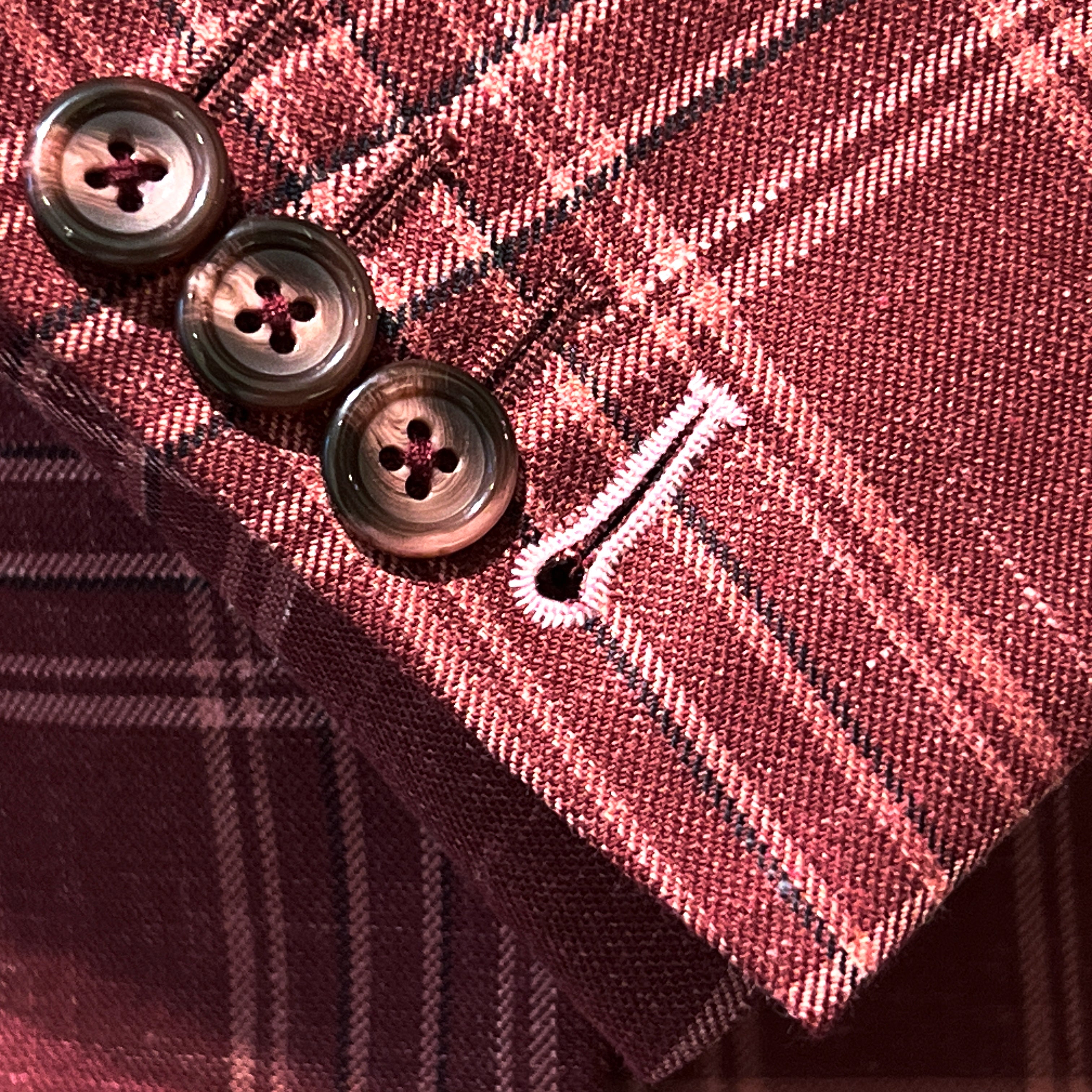 Sport coat sleeve cuff showing functional buttonholes with contrast white accent stitching on burgundy plaid fabric