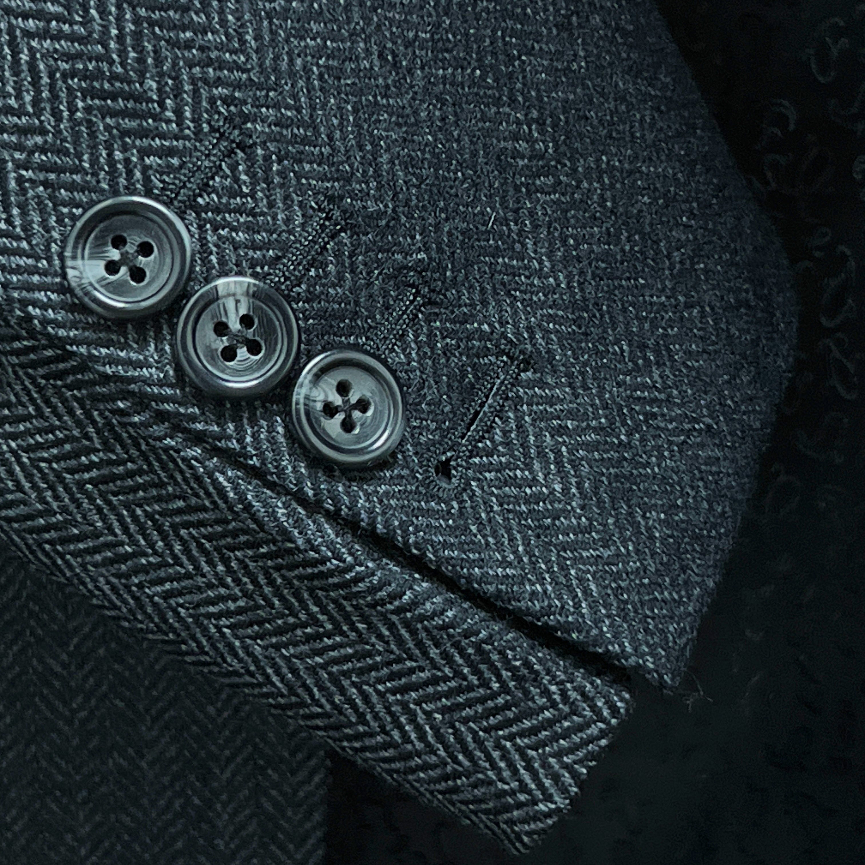 Sport coat sleeve cuff showing functional buttonholes with edge pick stitching on charcoal grey herringbone fabric
