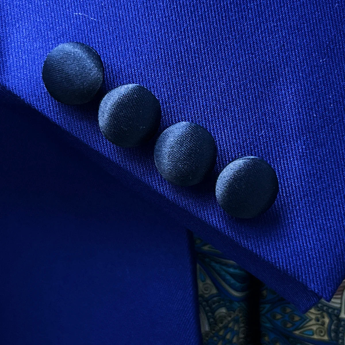 Close-up of functional buttonholes on the sleeve of a cobalt blue tuxedo jacket, showcasing fine tailoring and attention to traditional craftsmanship
