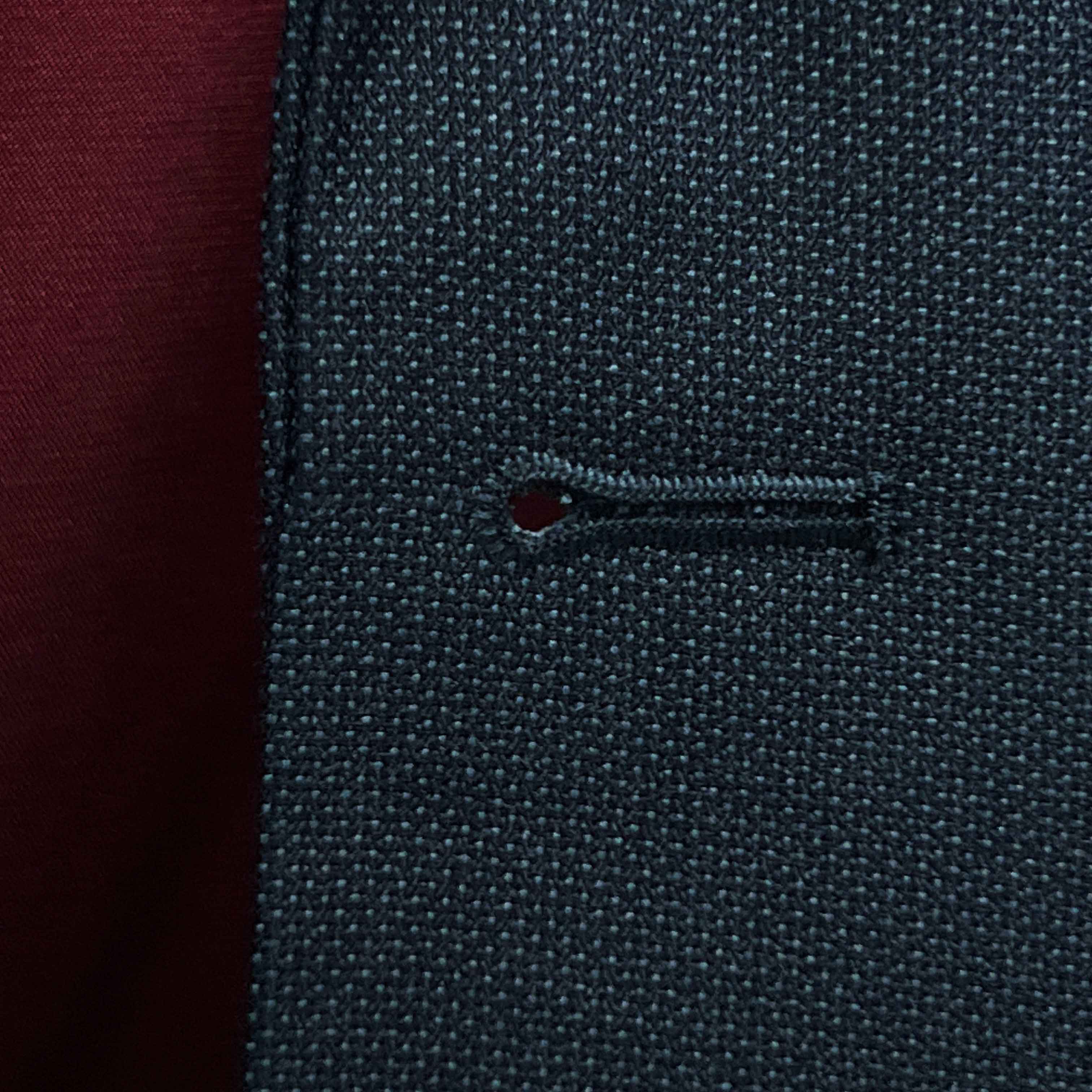 Detailed macro shot of hand-finished buttonhole stitching on dark charcoal grey birdseye suit with deep burgundy contrast thread