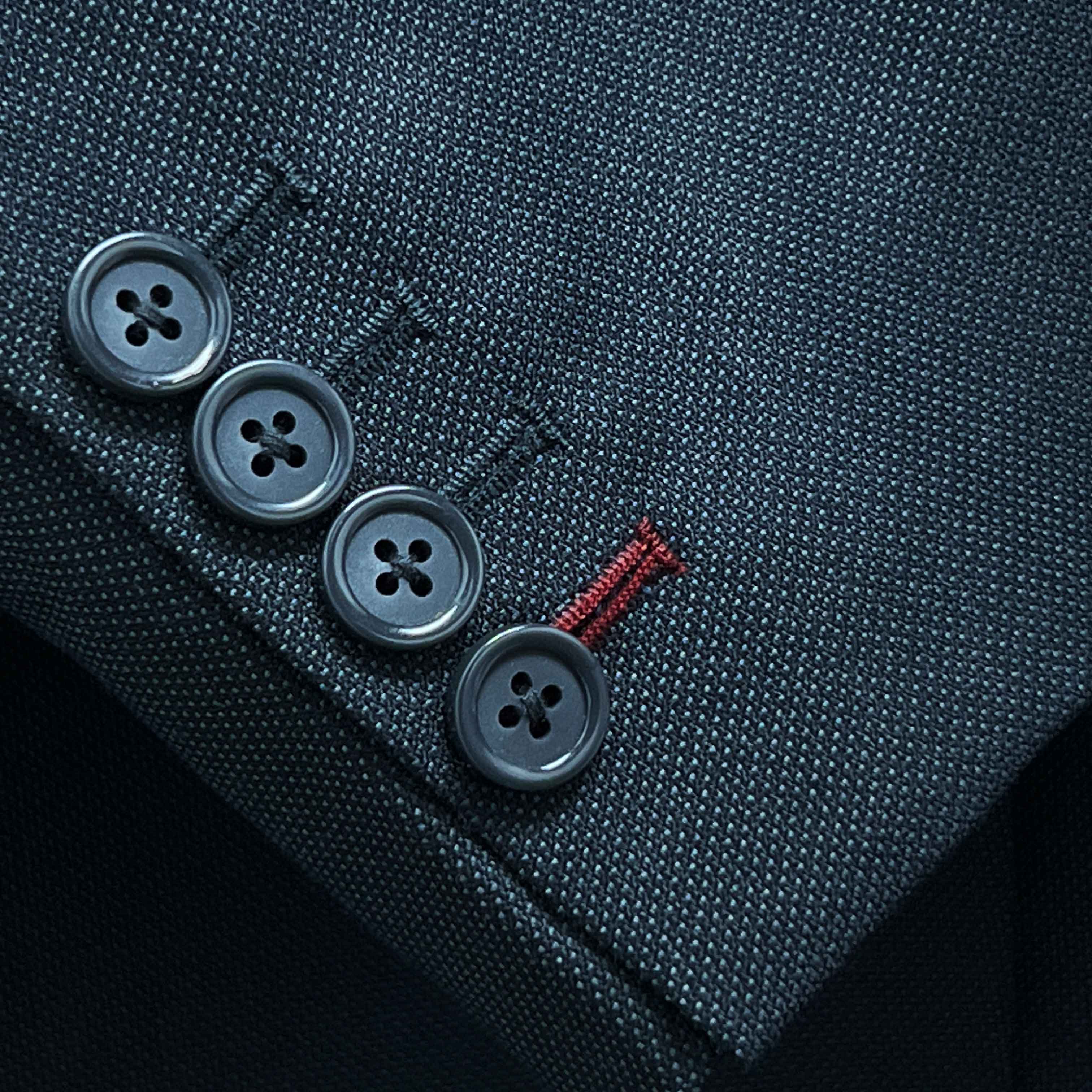 Suit jacket sleeve cuff showing functional buttonholes with contrast deep burgundy accent stitching on dark charcoal grey birdseye fabric
