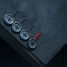 Suit jacket sleeve cuff showing functional buttonholes with contrast deep burgundy accent stitching on dark charcoal grey birdseye fabric