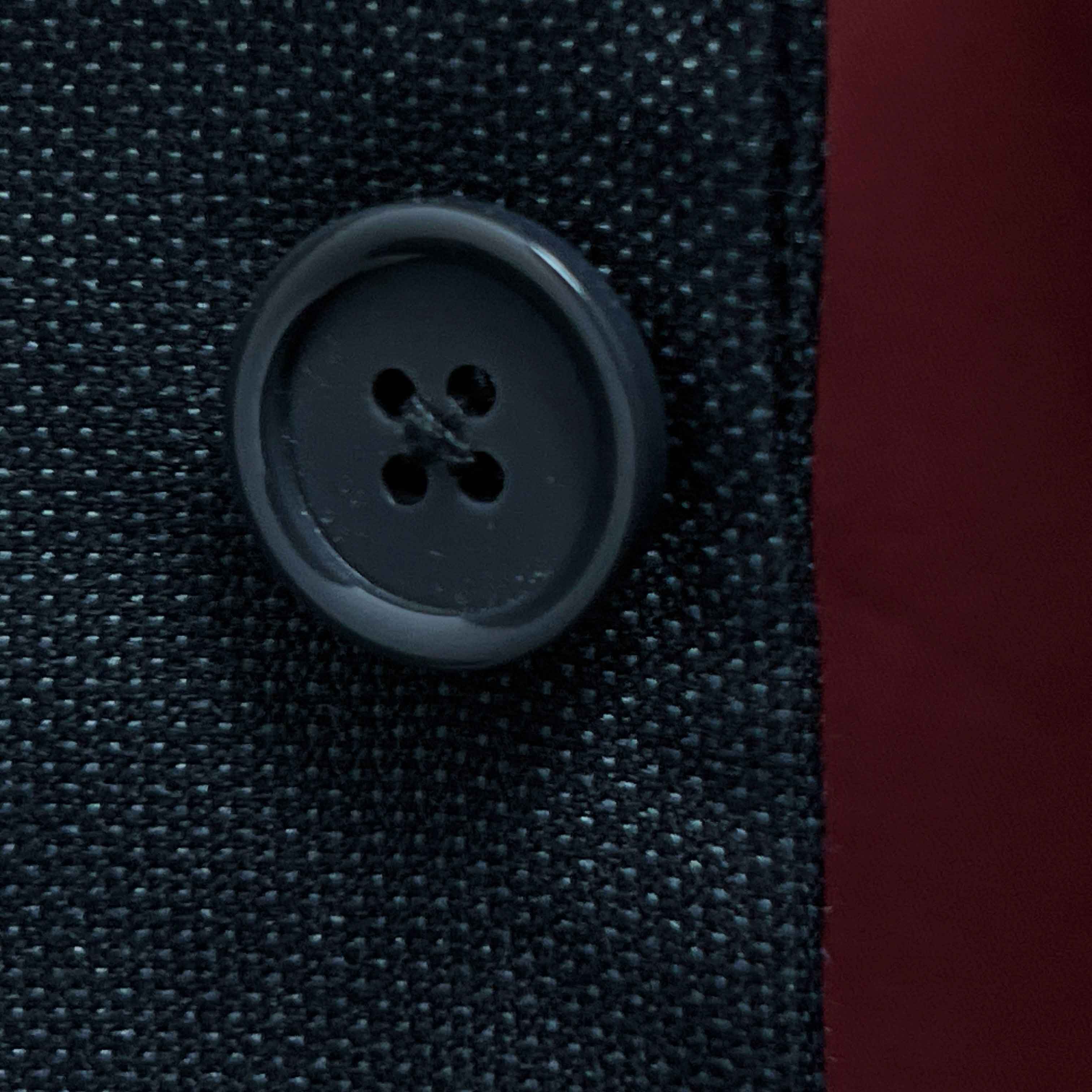 Close-up of dark grey horn buttons on dark charcoal grey birdseye suit jacket showing natural marble-like patterns