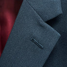 Classic notch lapel detail on dark charcoal grey birdseye suit jacket showing hand pick stitching and textured weave pattern