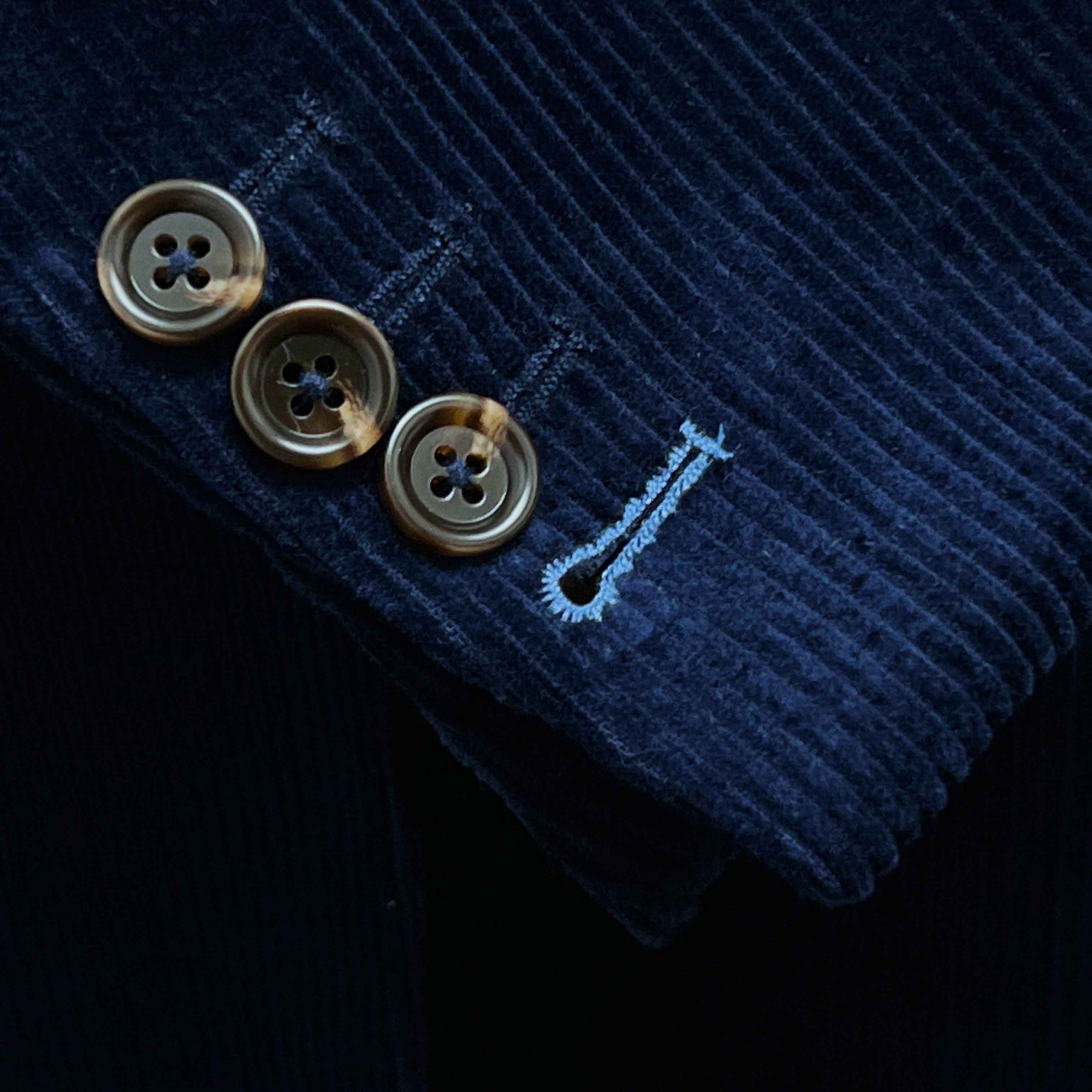 Sport coat sleeve cuff showing functional buttonholes with contrast light blue accent stitching on deep navy blue corduroy fabric